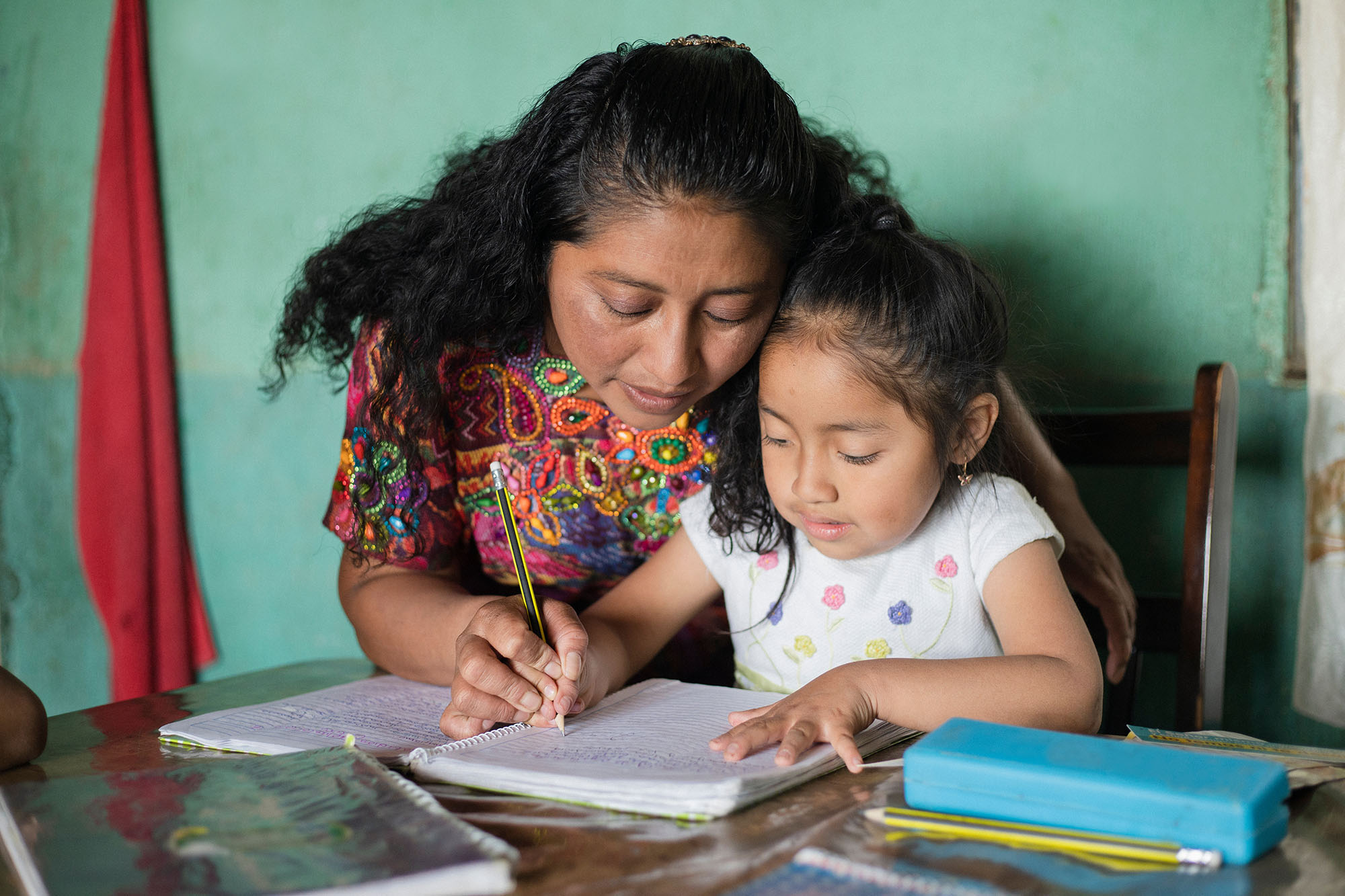 Hispanic mom helping her little daughter do her homework - Mom teaching her daughter to read and write at home - Mayan family at home
